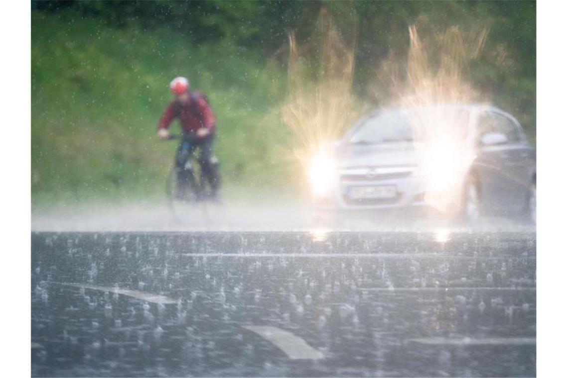 Ein Radfahrer fährt im prasselndem Regen neben einem Auto her. Foto: Lino Mirgeler