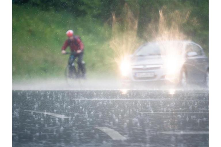 Ein Radfahrer fährt im prasselndem Regen neben einem Auto her. Foto: Lino Mirgeler
