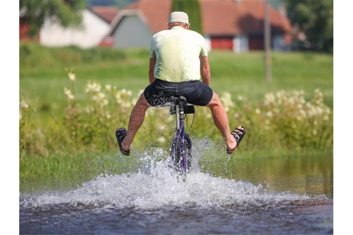 Ein Radfahrer fährt in Sandalen auf dem vom Regen überfluteten Donau-Radwanderweg durch das Hochwasser. Foto: Thomas Warnack/dpa