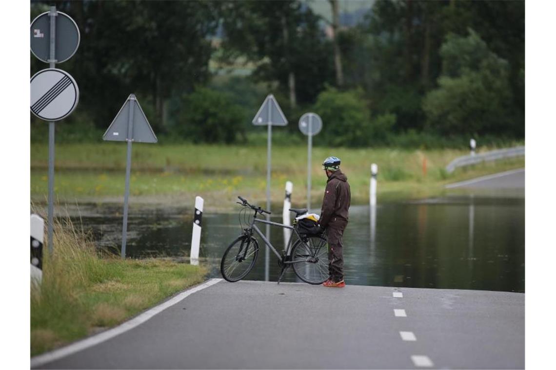 Hochwasser und Überflutungen nach neuem Starkregen Ein Radfahrer steht an einer überfluteten Straße. Foto: Thomas Warnack/dpa/Symbolbild