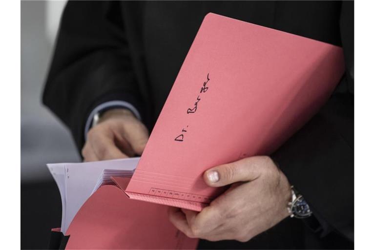 Ein Rechtsanwalt des Hauptbeschuldigten Hanno Berger hält vor dem Prozessauftakt um „Cum-Ex“-Aktiendeals im Gerichtssaal eine Akte mit der Aufschrift „Dr. Berger“ in der Hand. Foto: Boris Roessler/dpa