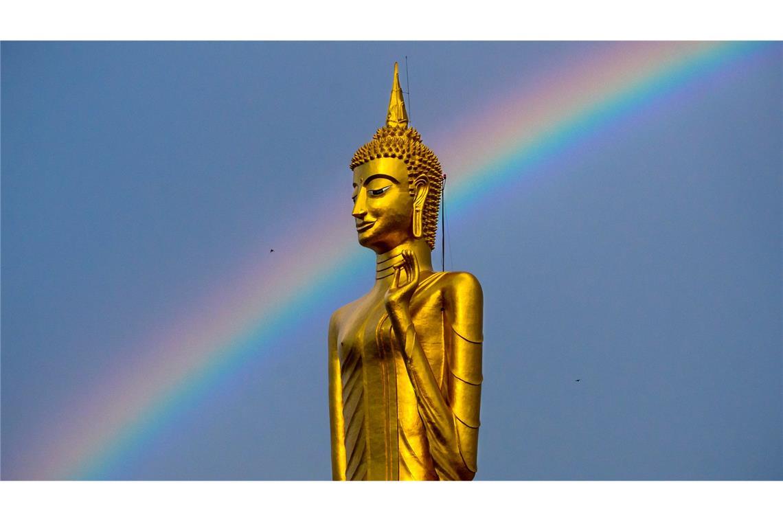 Ein Regenbogen ist hinter der stehenden Buddha-Statue Luang Pho Yai des Wat Buraphaphiram in Roi Et, Thailand, zu sehen.