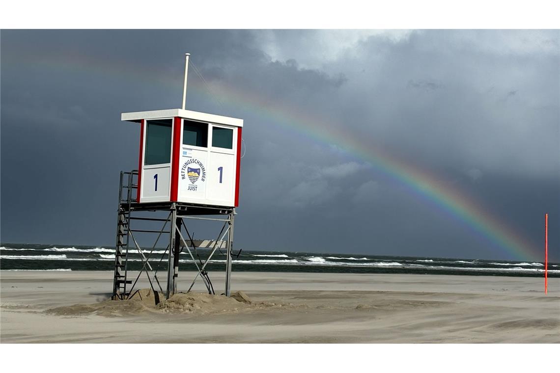 Ein Regenbogen steht an einem Himmel voll dunkler Wolken über der Nordsee und über der Insel Juist.