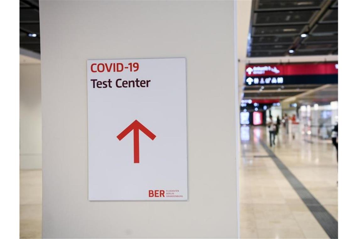 Ein Reisender geht im Flughafen Berlin-Brandenburg (BER) mit einem Koffer nahe eines Hinweisschildes mit der Aufschrift „Covid-19 Test Center“. Foto: Jens Kalaene/dpa-Zentralbild/dpa