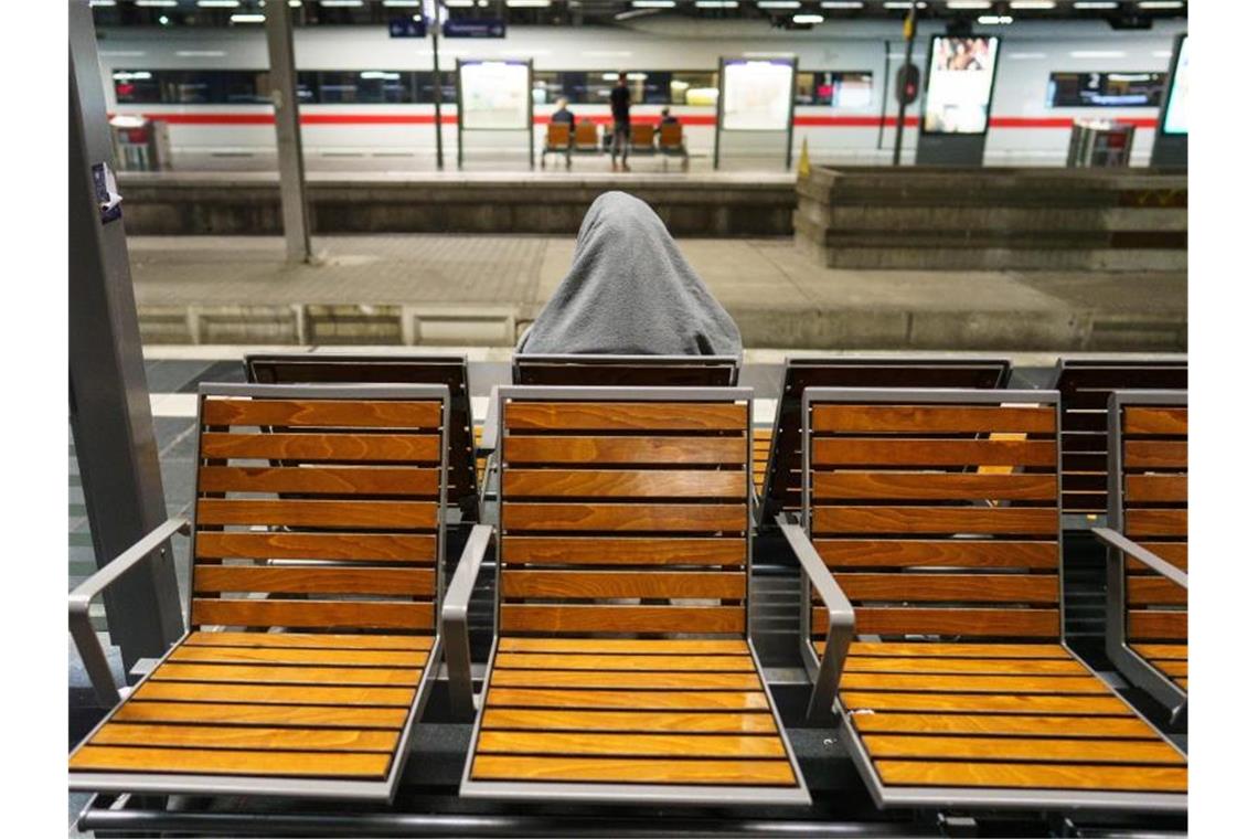 Ein reisender sitzt am frühen Morgen mit einer Decke über dem Kopf an einem Gleis im Frankfurter Hauptbahnhof. Foto: Frank Rumpenhorst/dpa