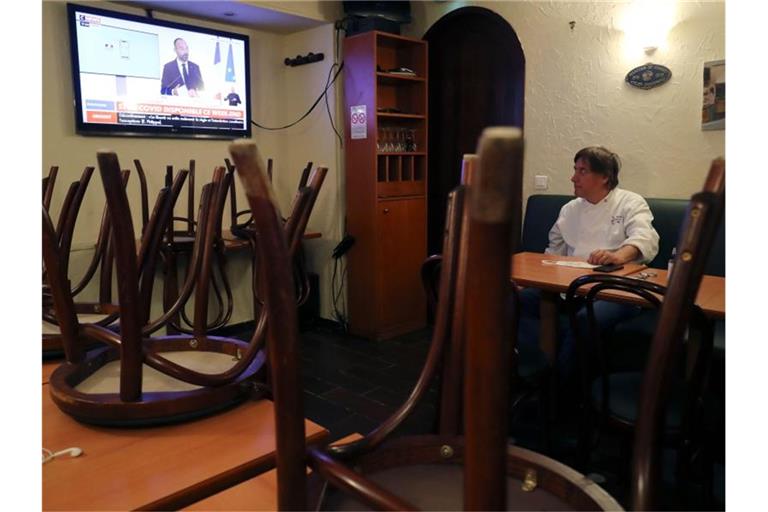 Ein Restaurantbesitzer schaut sich in Paris auf einem Nachrichtensender eine Fernsehansprache des französischen Premierministers Philippe an. Foto: Ludovic Marin/AFP/dpa