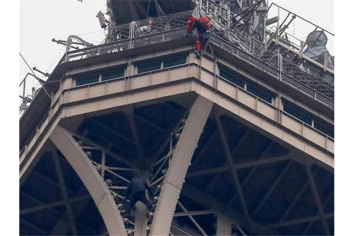 Ein Rettungshelfer (oben in roter Berufskleidung) klettert angeseilt am Eiffelturm hinunter, während unter ihm der Kletterer an die Gitterstäbe klammert. Foto: Michel Euler/AP
