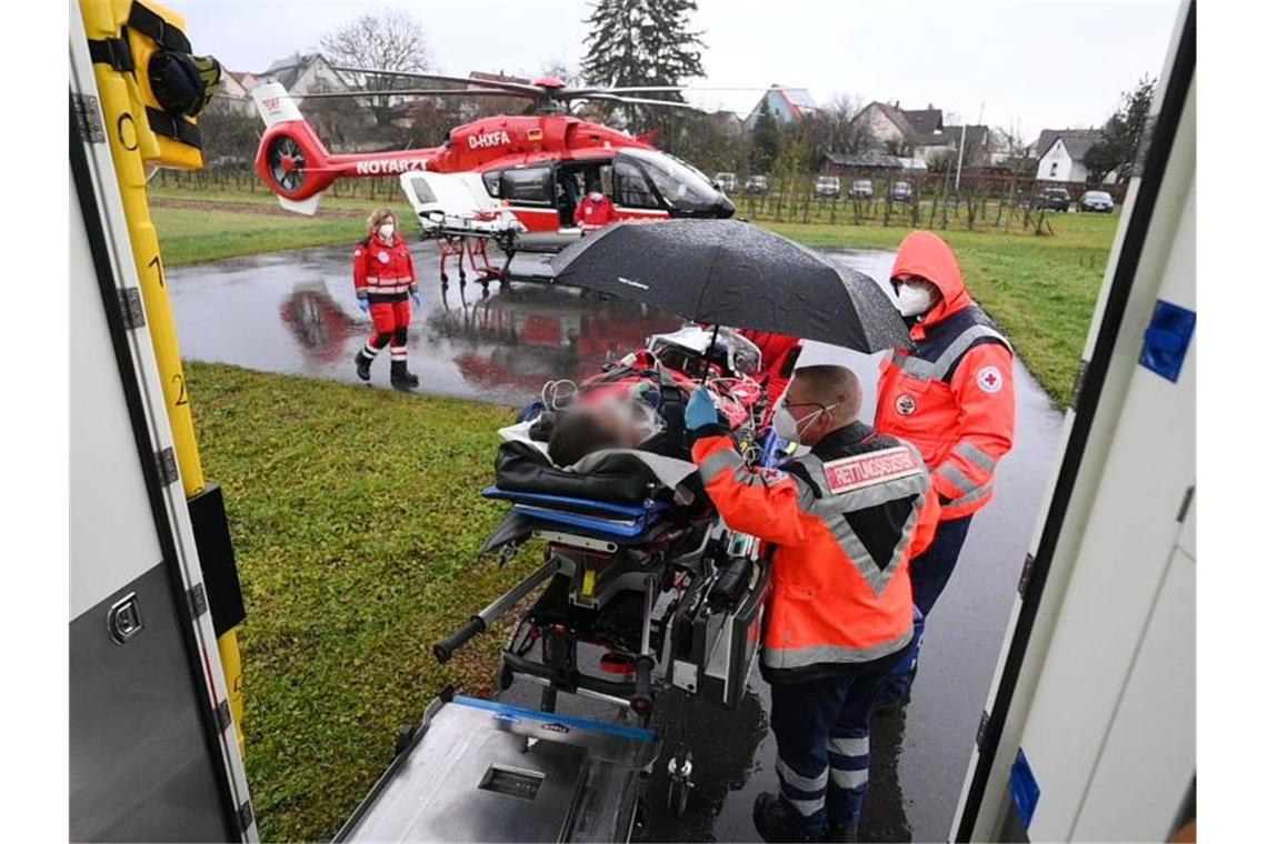 Platz auf Intensivstationen: Luftrettung verlegt Patienten Ein Rettungssanitäter hält einen Schirm über einen Patienten, der von einem Rettungwagen zu dem Rettungshubschrauber für den Weitertransport gebracht wird. Foto: Marijan Murat/dpa
