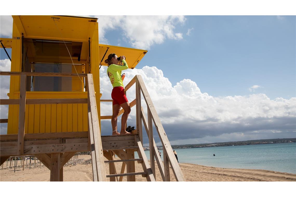 Ein Rettungsschwimmer benutzt ein Fernglas, während er am Strand von Palma auf Mallorca patrouilliert.