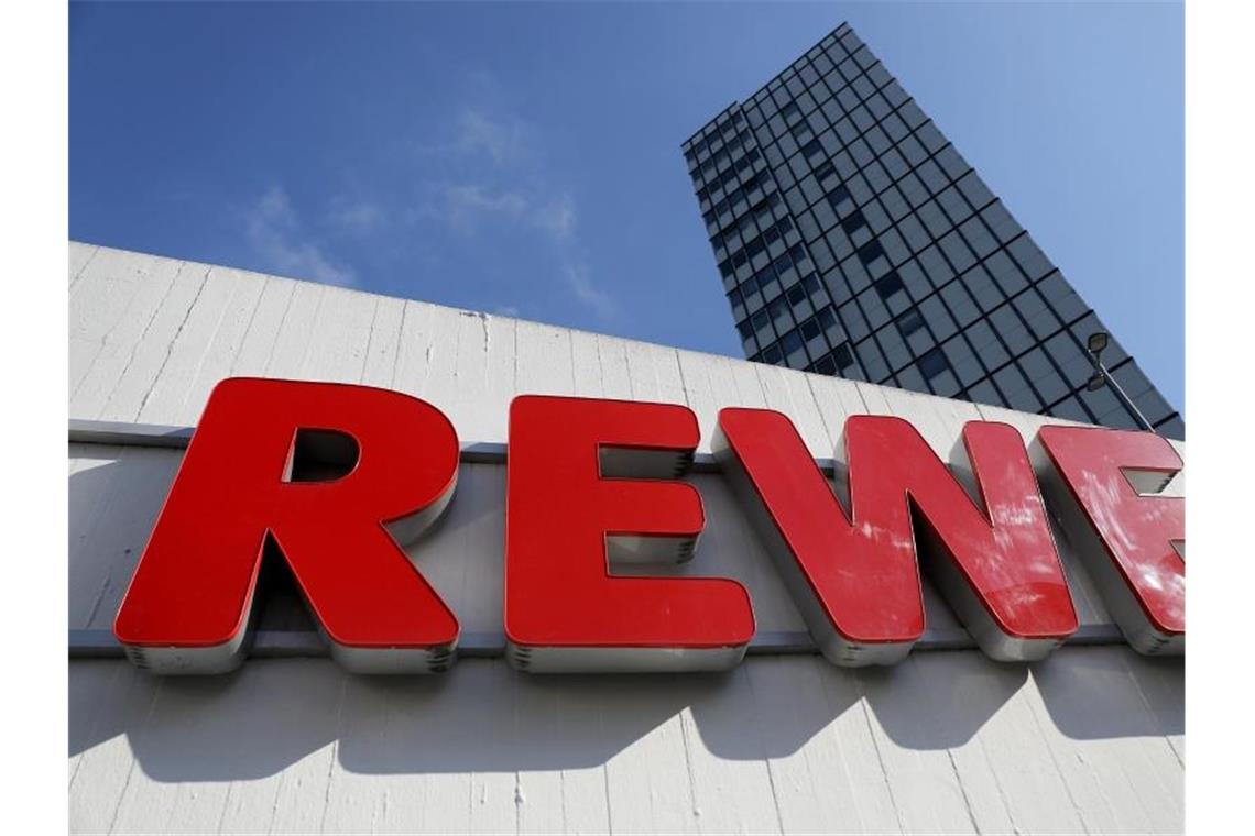 Ein Rewe Schriftzug hängt vor einem Supermarkt. Foto: Oliver Berg/dpa