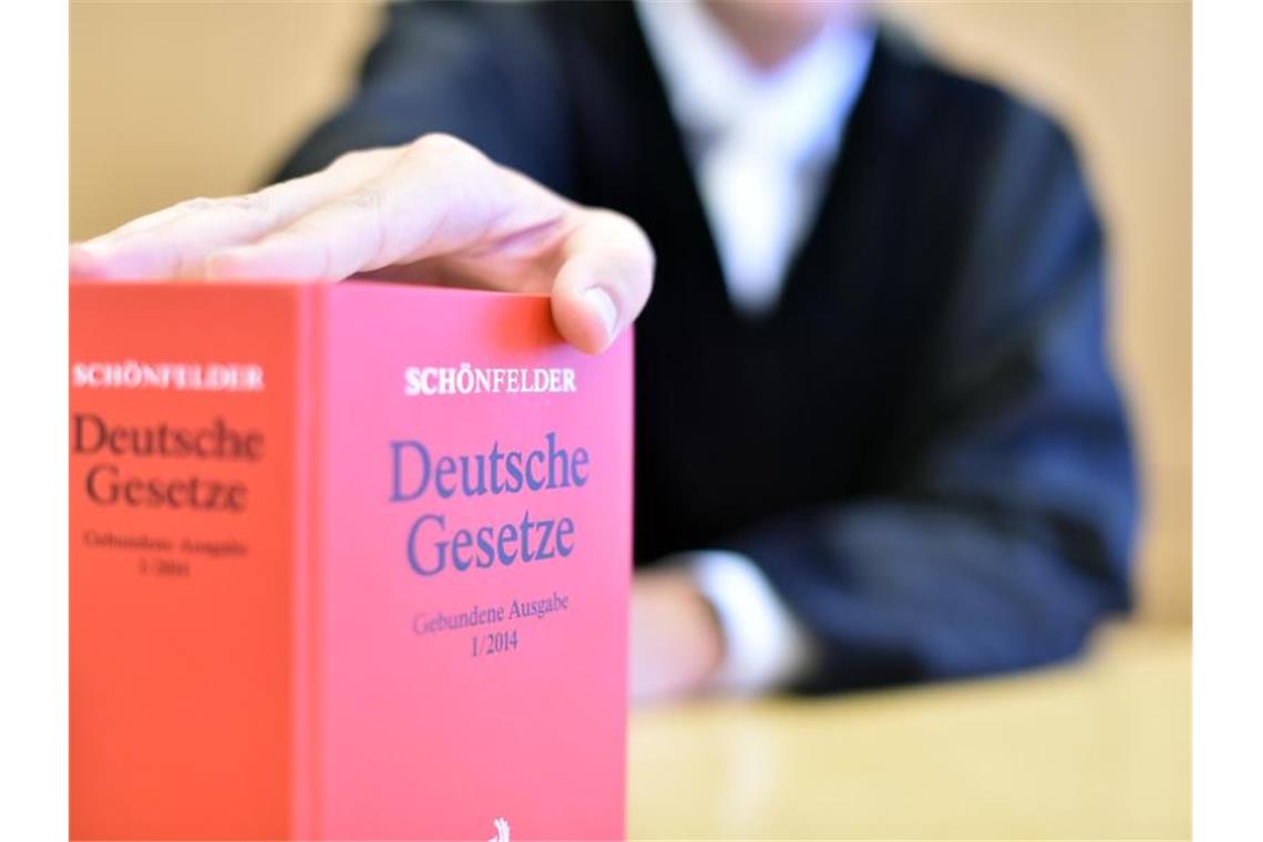 Ein Richter legt seine Hand auf ein Buch mit Deutschen Gesetzen. Foto: picture alliance / dpa/Illustration