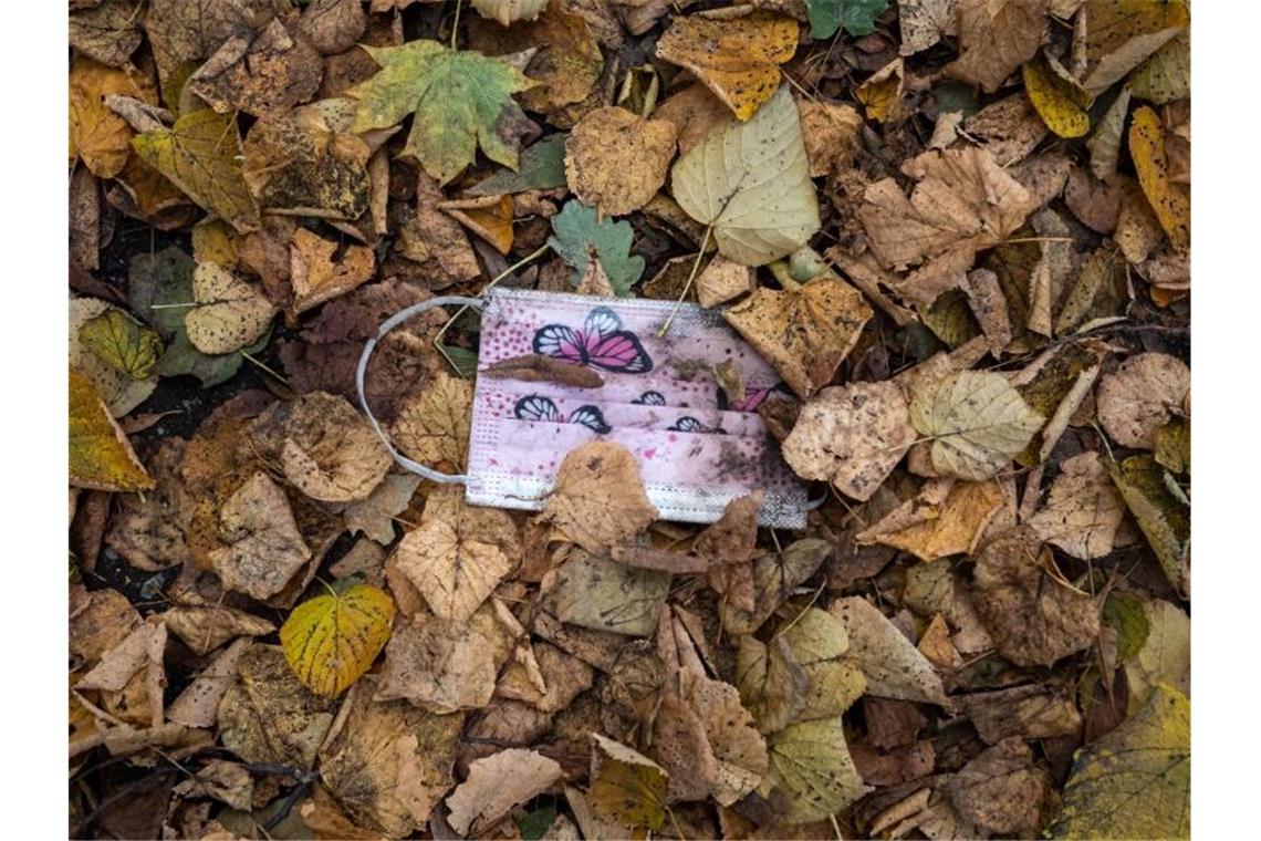 Ein rosafarbener Mund-Nasen-Schutz gegen das Virus im Herbstlaub. Foto: Peter Kneffel/dpa