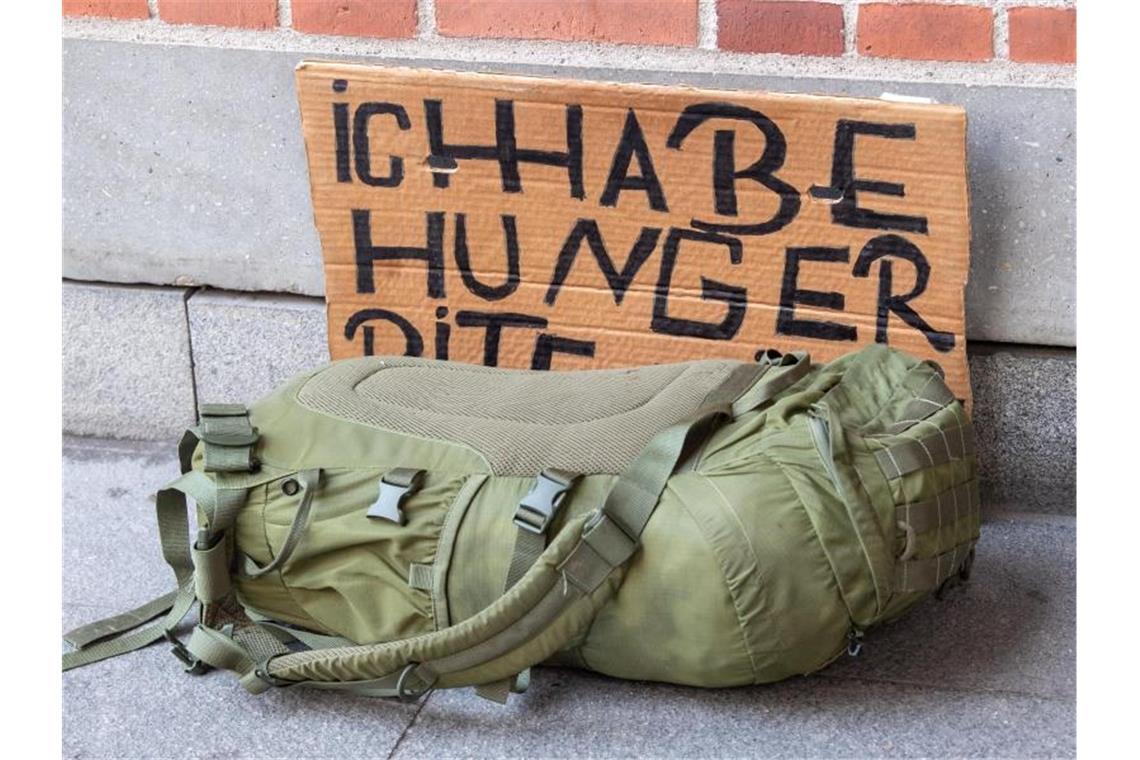 Ein Rucksack liegt vor einem Pappschild mit der Aufschrift „Ich habe Hunger“ an einer Hausecke. Foto: Peter Kneffel/dpa