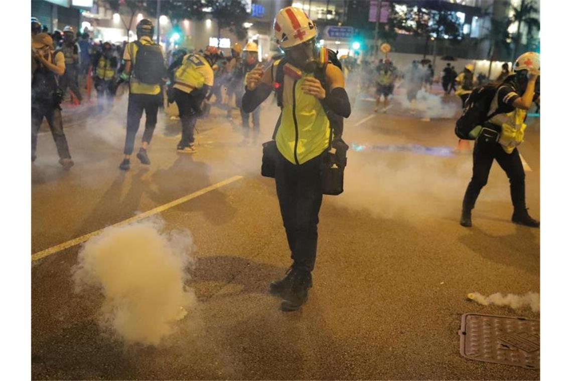 Ein Sanitäter unter den Demonstranten reagiert trotz Atemmaske auf das Tränengas der Polizei. Foto: Kin Cheung/AP/dpa