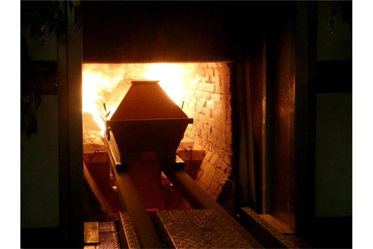 Ein Sarg wird in den rund 850 Grad heißen Krematoriumsofen gefahren. F. Foto: Roland Weihrauch/dpa