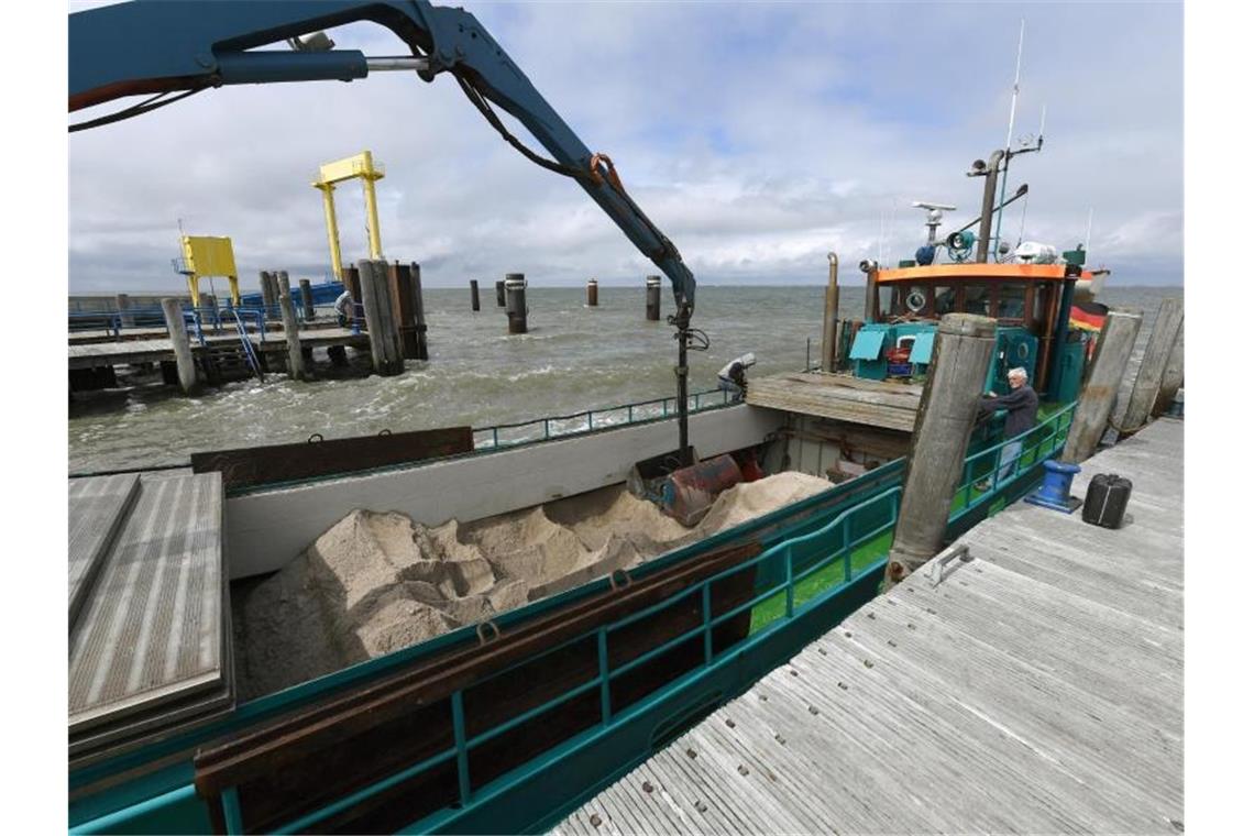 Ein Schiff mit Sand zur Erhöhung der Warften wird am Anleger der Hallig Hooge entladen. Foto: Carsten Rehder/dpa