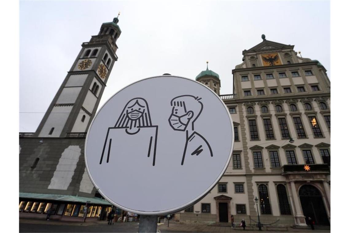 Ein Schild auf dem Rathausplatz in Augsburg weist auf Maskenpflicht hin. Foto: Karl-Josef Hildenbrand/dpa