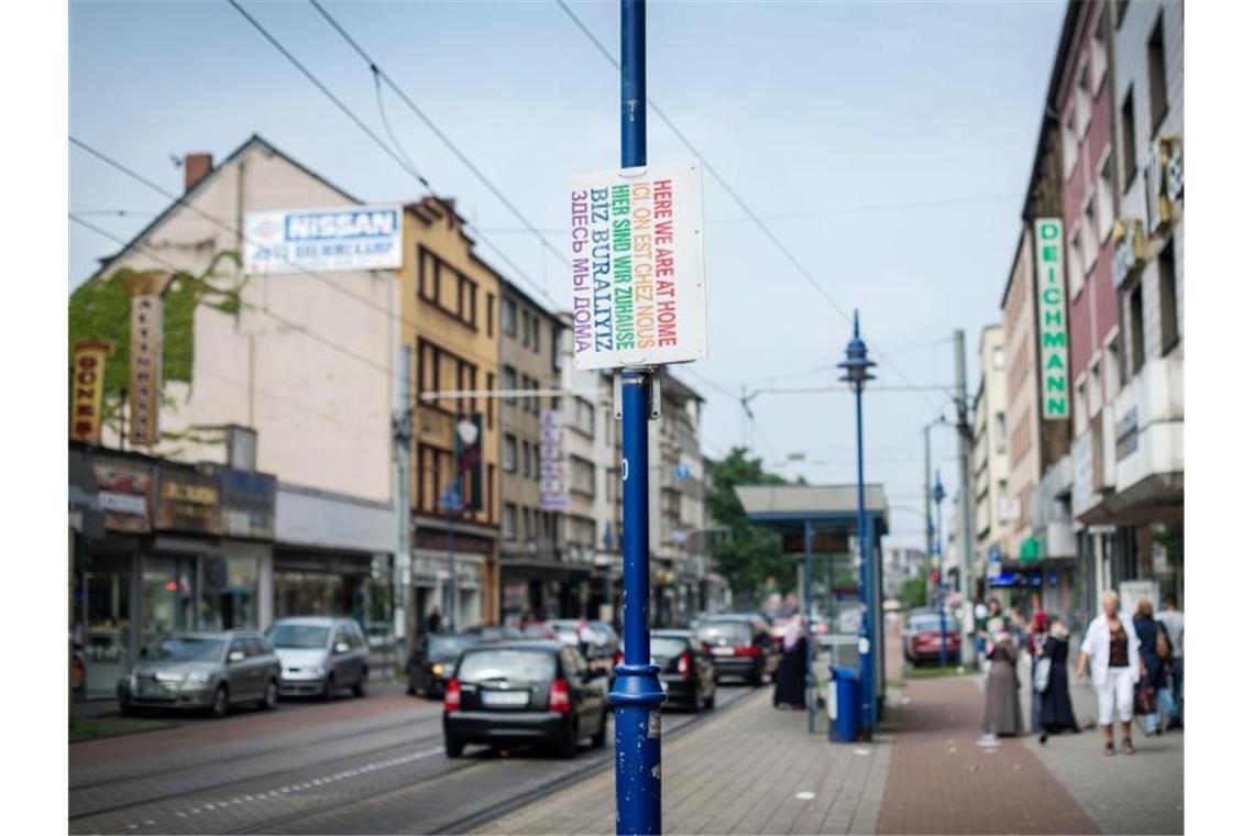 Ein Schild „Hier sind wir zuhause“ in verschiedenen Sprachen hängt in Duisburg auf der Straße. Foto: picture alliance / dpa