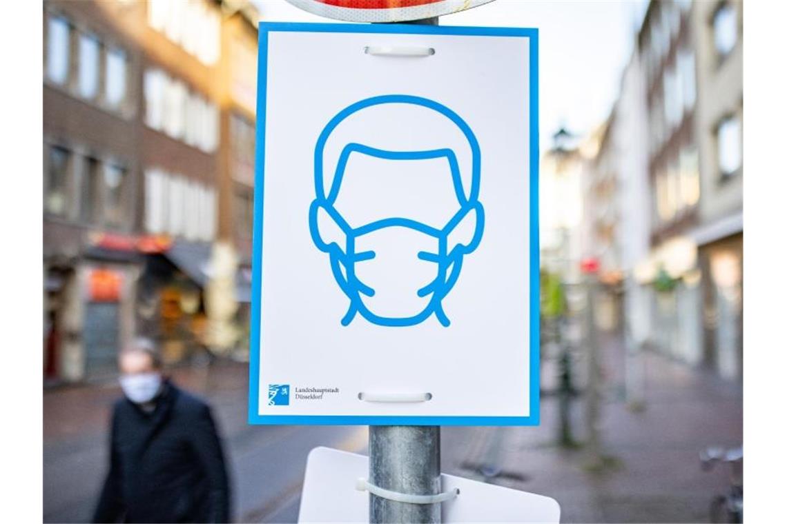 Ein Schild mit dem Symbol für Maskenpflicht an einem Straßenschild in der Innenstadt von Düsseldorf. Foto: Marcel Kusch/dpa