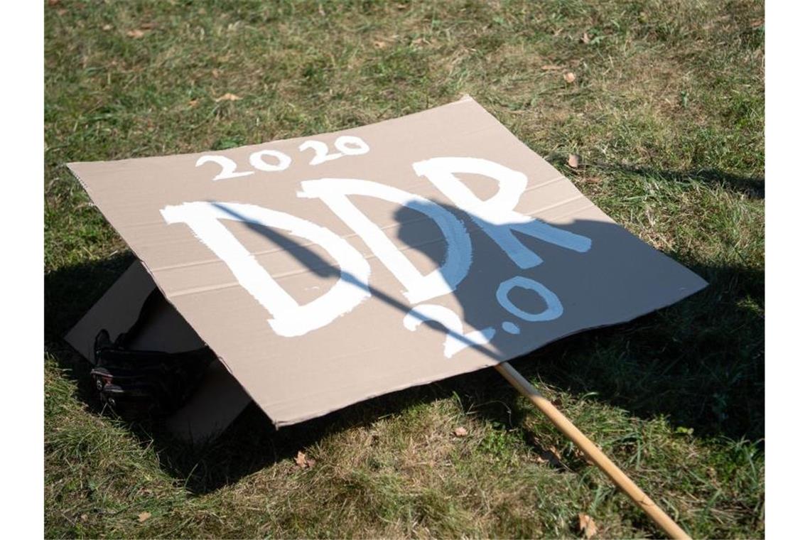 Ein Schild mit der Aufschrift „2020 DDR 2.0“ liegt während einer Kundgebung der Initiative „Querdenken 711“ im Stuttgarter Schlossgarten. Foto: Sebastian Gollnow/dpa