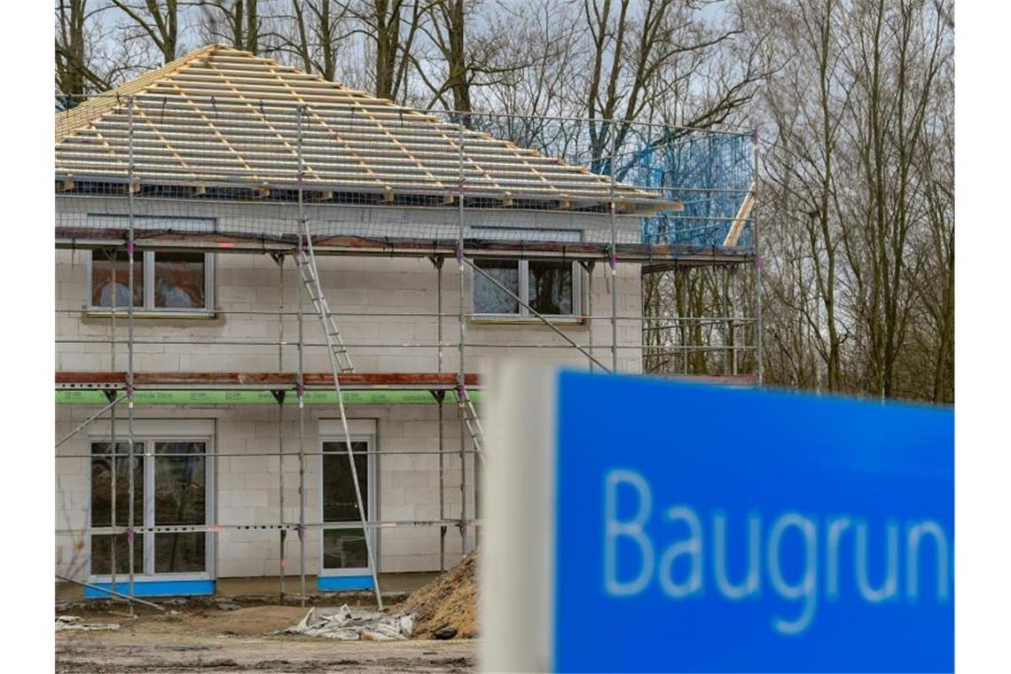 Ein Schild mit der Aufschrift „Baugrundstücke“ steht am Rande eines Baufeldes mit einem Rohbau eines Eigenheimes. Foto: Patrick Pleul/zb/dpa