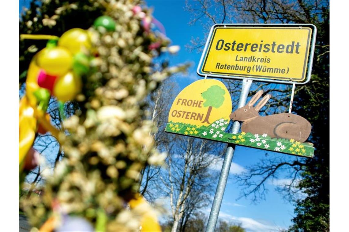 Ein Schild mit der Aufschrift "Frohe Ostern" hängt unter dem Ortsschild am Ortseingang von Ostereistedt. Foto: Hauke-Christian Dittrich/dpa