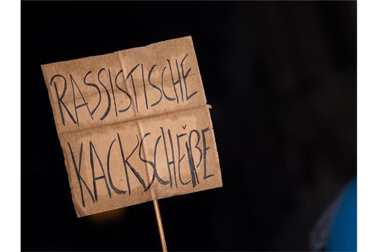 Ein Schild mit der Aufschrift "Rassistische Kackscheiße" wird auf einer Demonstration in die Höhe gehalten. Foto: Sebastian Gollnow/dpa/Archivbild