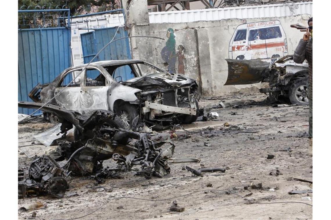 Ein schwer bewaffneter Soldat steht nach dem Anschlag neben Überresten von Fahrzeugen. Foto: Farah Abdi Warsameh/AP/dpa