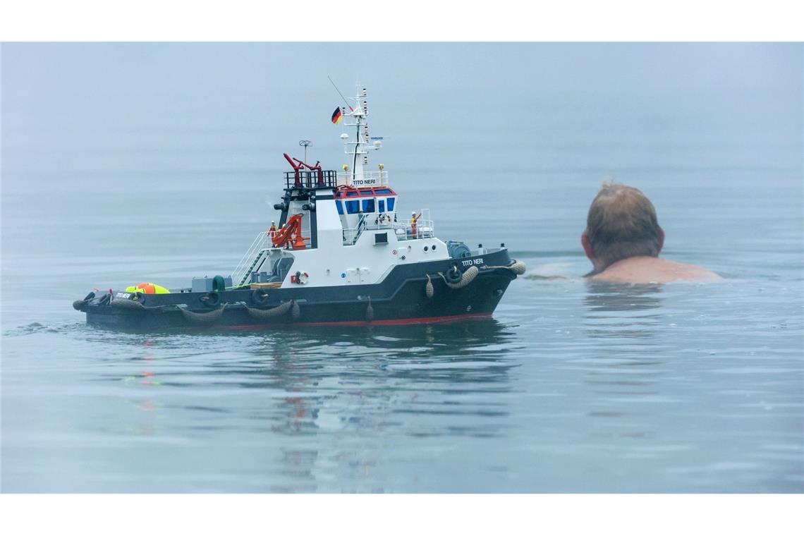 Ein Schwimmer und ein Modellboot in Form eines Schleppers sind im Nebel im Schwarzachtalsee unterwegs.