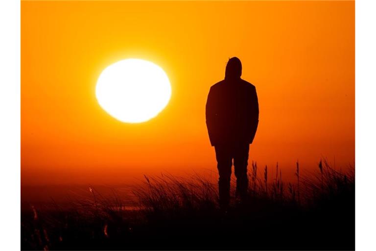 Ein Spaziergänger genießt am Strand von Schillig in Niedersachsen den Sonnenaufgang. Foto: Sina Schuldt/dpa