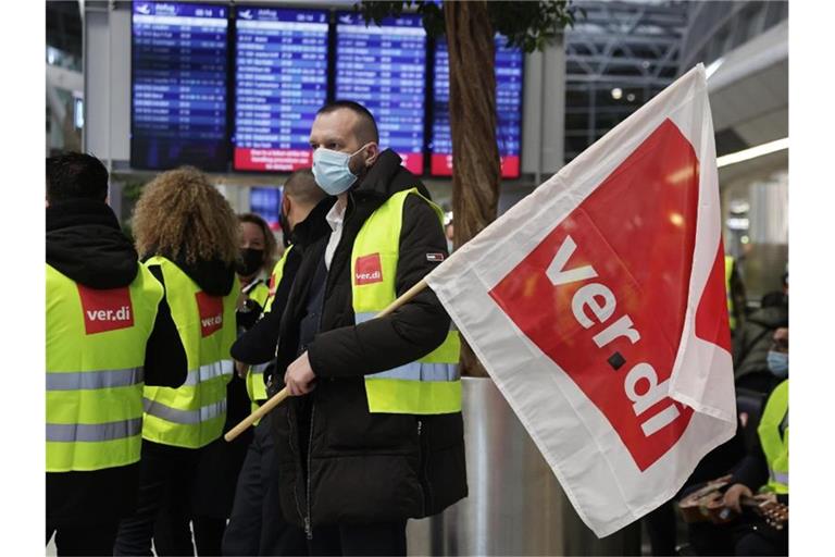 Ein Streikender hält auf einem Flughafen eine Verdi-Flagge. Foto: David Young/dpa