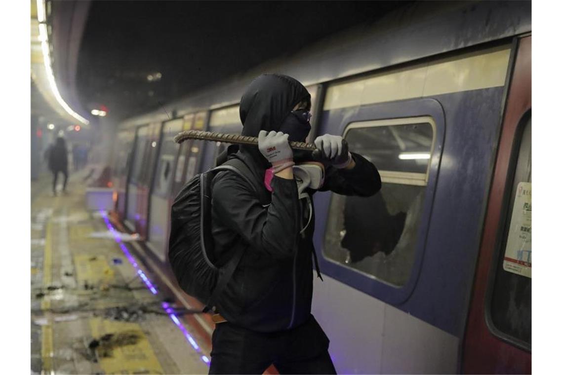 Demonstranten legen Hongkong lahm - Gewalt eskaliert weiter Ein Student demoliert die Scheiben eines Zuges, der in der MTR-Station der chinesischen Universität hält. Foto: Kin Cheung/AP/dpa