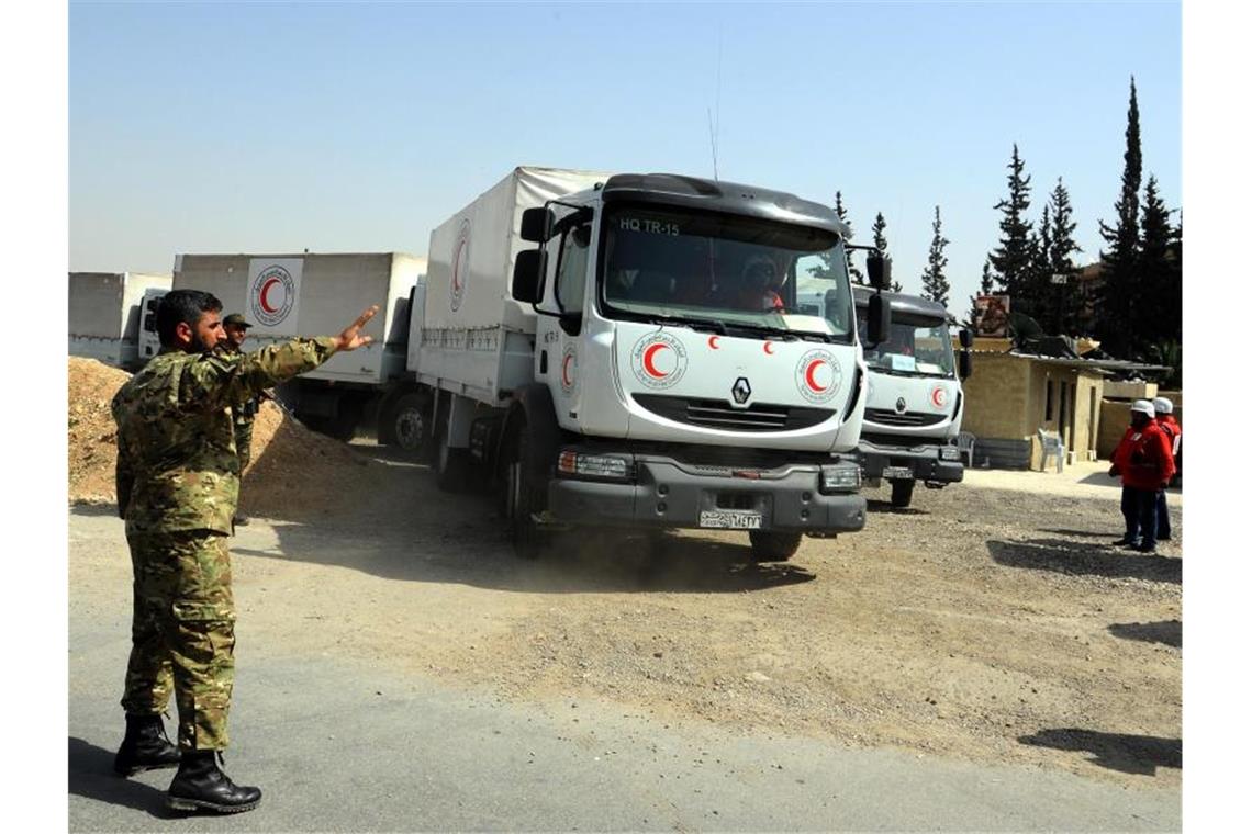 Ein syrischer Soldat weist Lastwagen des Syrisch-Arabischen Roten Halbmondes mit Hilfsgütern in Richtung eines umkämpften Gebiets (Archiv). Foto: Ammar Safarjalani/Xinhua/dpa