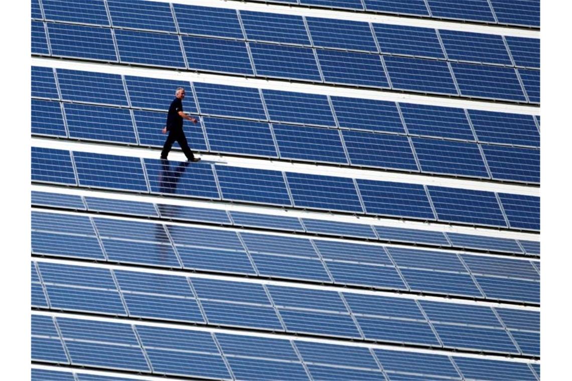 Ein Techniker läuft über ein Dach auf dem eine Photovoltaik-Anlage montiert wurde. Foto: Jens Büttner/dpa-Zentralbild/dpa