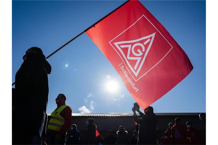 Ein Teilnehmer eines Warnstreiks schwenkt eine Fahne mit dem Logo der IG Metall. Foto: Nicolas Armer/dpa/Symbolbild