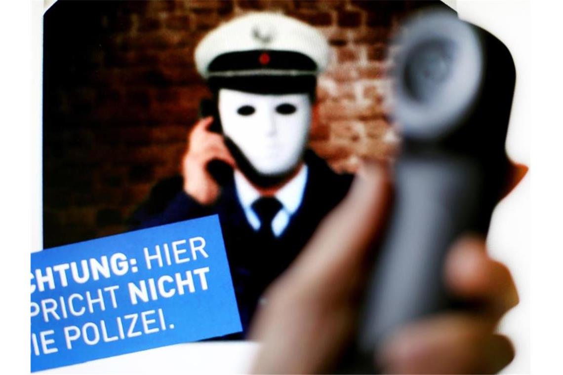 Ein Telefonhörer ist vor einem Plakat der Polizei mit der Aufschrift „Achtung: Hier spricht nicht die Polizei“ zu sehen. Foto: Martin Gerten/Archiv