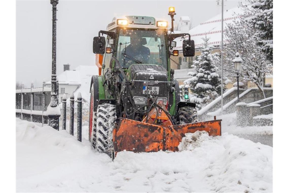 Ein Traktor mit Schneepflug räumt eine verschneite Straße im Ortskern der Ortschaft am Tegernsee. Foto: Peter Kneffel/dpa