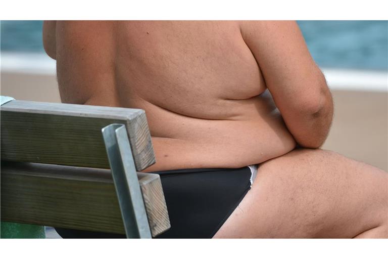 Ein übergewichtiger Mann sitzt in einem Freibad.