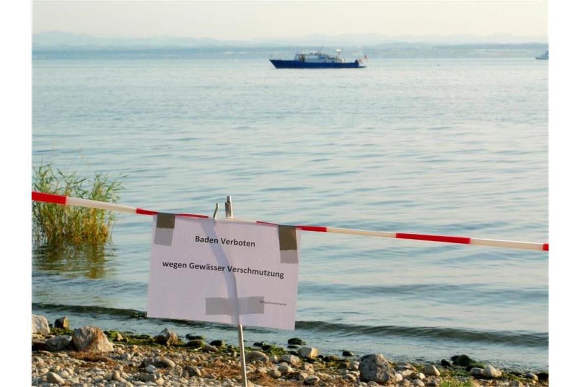 Ein Uferabschnitt am Bodensee bei Friedrichshafen ist mit einem Hinweisschild und einem Absperrband für Badegäste gesperrt. Foto: Marcus Fey