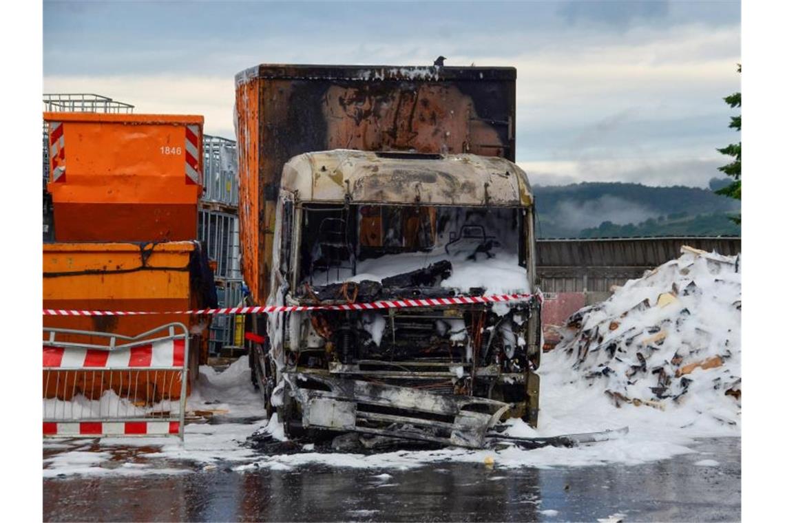 Ein verbrannter Lkw steht, bedeckt von Löschschaum, neben einem Container einer Recyclingfirma. Foto: Andreas Rosar/Fotoagentur Stuttgart/dpa