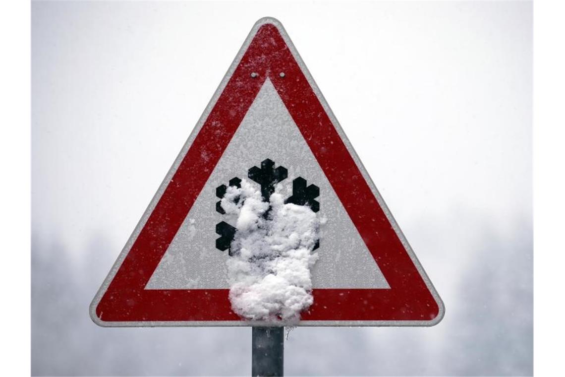 Ein Verkehrsschild, auf dem vor Schnee- und Eisglätte gewarnt wird, ist mit Schnee bedeckt. Foto: Karl-Josef Hildenbrand/dpa/Archivbild