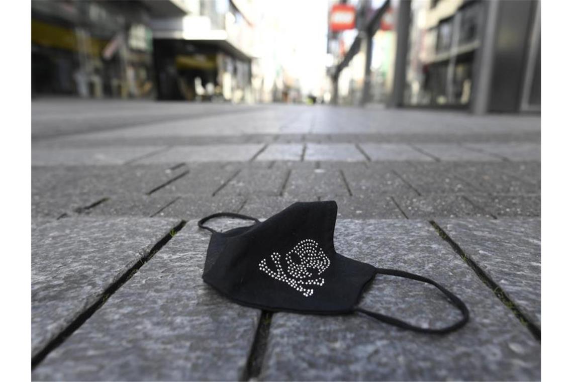 14.611 Fälle: Corona-Neuinfektionen unter Vorwochenniveau Ein verlorener Mundschutz liegt auf einer Einkaufsstraße. Foto: Roberto Pfeil/dpa/Symbolbild/Archiv