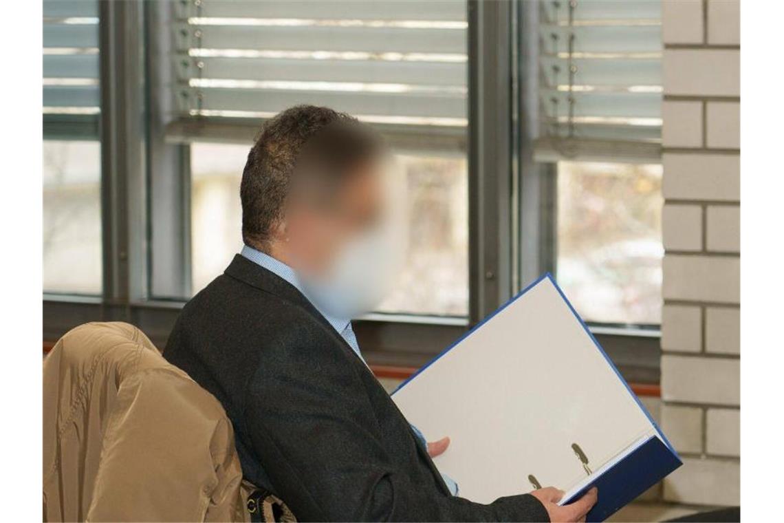 Ein wegen sexuellen Missbrauchs von Patientinnen angeklagter Arzt liest in einem blauen Ordner. Foto: Benedikt Spether/dpa