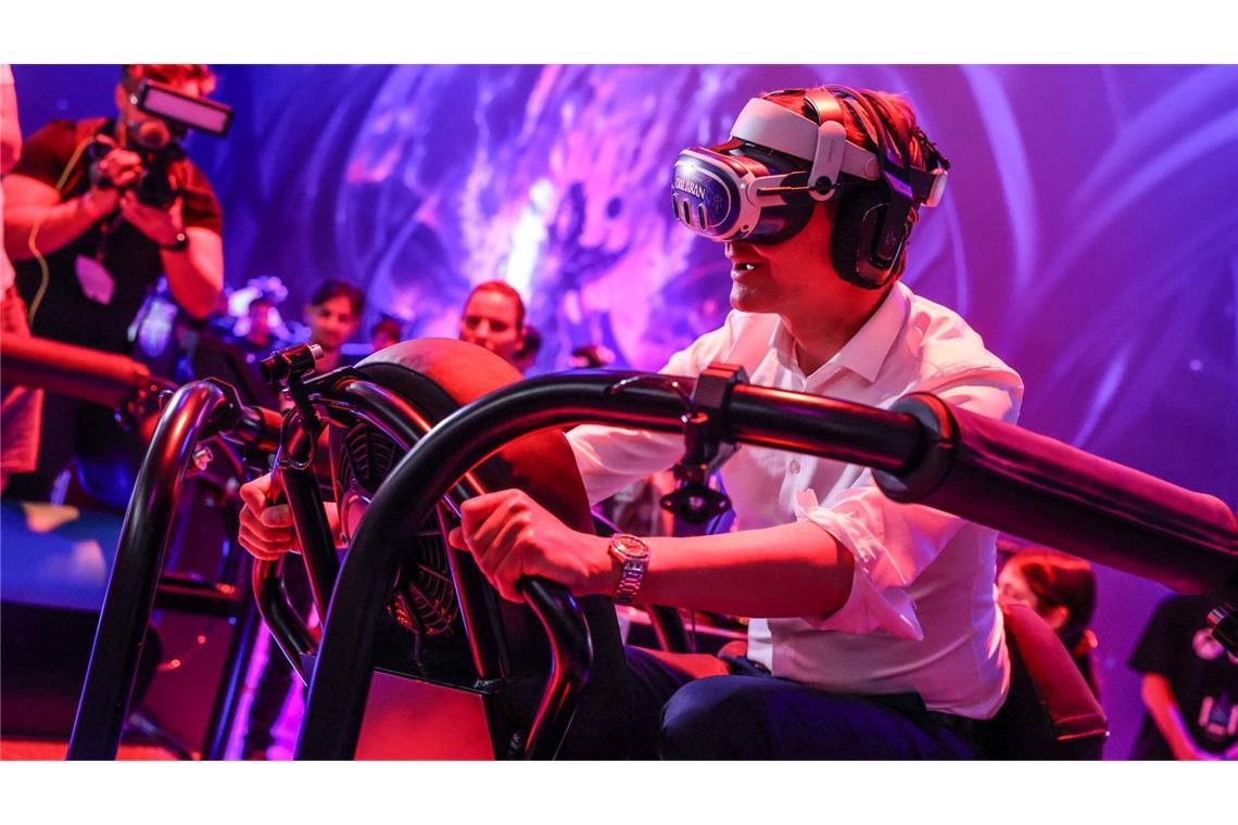Ein wilder Ritt bei der Gamescom 2024: Hendrik Wüst auf einem "Drachen", genauer gesagt mit virtueller Brille auf einem schwankenden Gestell.