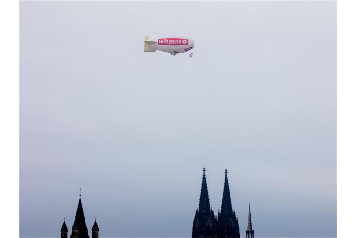 Ein Zeppelin mit der Aufschrift „bliev zohuss“ (Bleib zu Hause) der Roten Funken fliegt über den Kölner Dom. Wegen der Corona-Pandemie ist der Auftakt der Karnevalssaison abgesagt. Foto: Rolf Vennenbernd/dpa