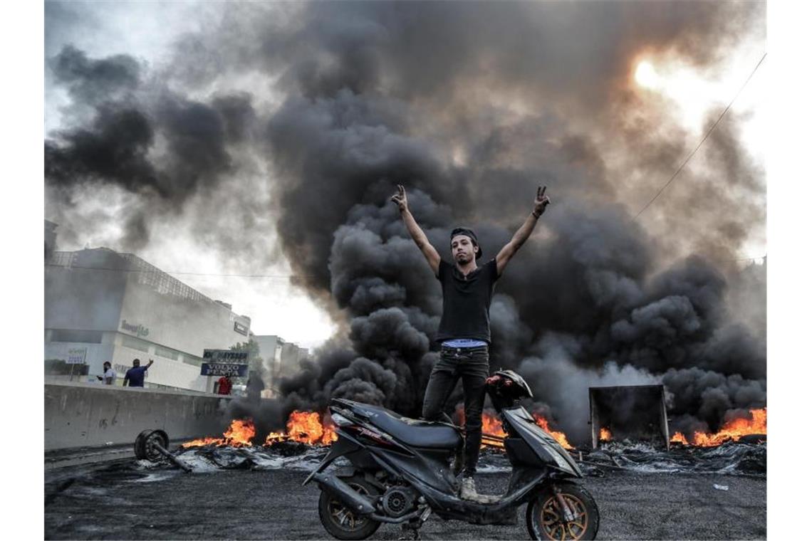 Ein Demonstrant steht in Beirut auf einem Motorroller und gestikuliert vor einer Barrikade. Foto: Marwan Naamani/dpa