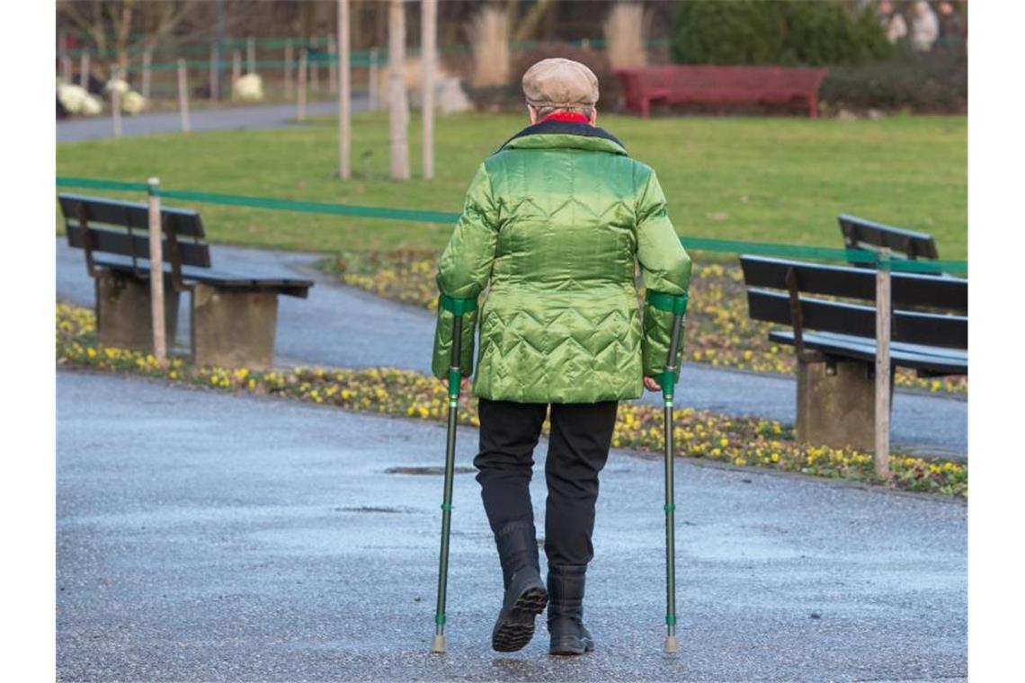 Eine ältere Frau geht mit Gehhilfen durch einen Park. Foto: Armin Weigel/dpa