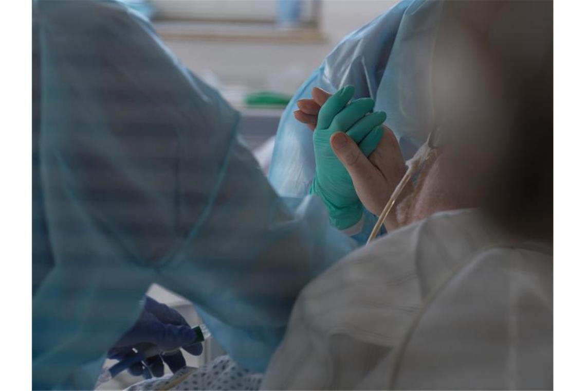 Eine Ärztin hält in einer Intensivstation die Hand eines Coronapatienten. Foto: Henning Kaiser/dpa/Symbolbild