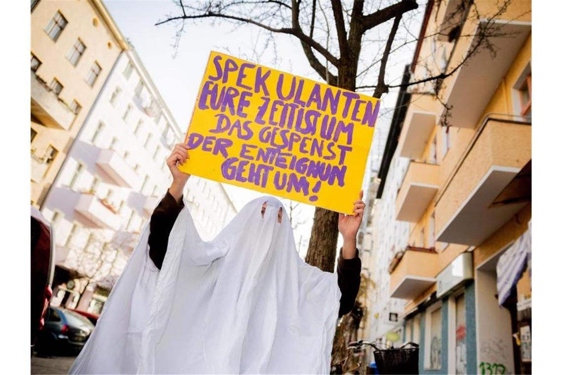 Volksbegehren zur Enteignung von Wohnkonzernen gestartet Eine Aktivistin im Gespensterkostüm hält ein Protestschild nahe dem Organisationsbüro des Volksbegehrens „Deutsche Wohnen & Co. enteignen“ in die Kamera. Foto: Christoph Soeder/dpa