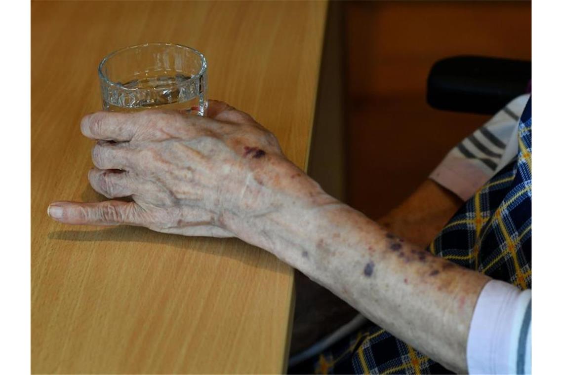 Eine alte Frau greift nach einem Glas Wasser. Foto: Jens Kalaene/dpa-Zentralbild/dpa/Archivbild